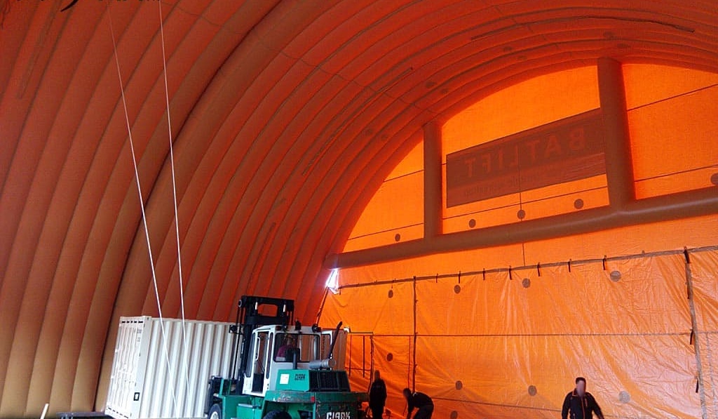 Interior view of a large inflatable shelter of very large dimensions and surfaces, in 0.45 mm double-skin padded PVC envelope, with a military vehicle in the process of dropping off a maritime container.