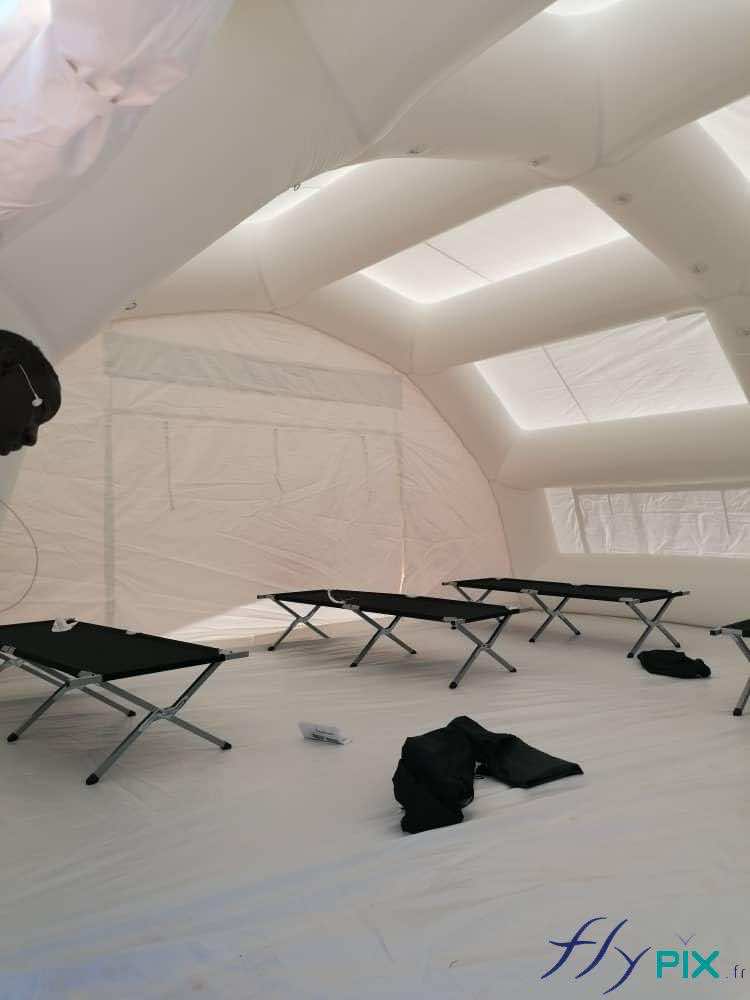 A general view of the interior of the inflatable medical shelter, a first aid station, with cots deployed on the floor by the SAMU (Emergency Medical Service) medical personnel. At the far end, a large, wide gable door serves as the exit. A removable protective tarpaulin covering 60 square meters covers the floor. – Copyright Vivien LAÏLLE / FlyPix – All rights reserved, reproduction prohibited.