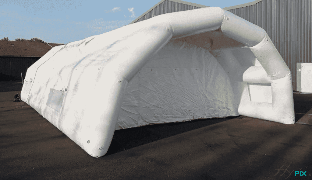 A general view of the front gable end of the PMA inflatable tent, featuring a large canopy and a main access door with a ground flap. The tent is a semi-circular tunnel type. In this case, the canopy provides weather protection for stretchers and personnel (victims, patients, or accident victims) during unloading from the rear of the rescue vehicle. – Copyright Vivien LAÏLLE / FlyPix – All rights reserved, reproduction prohibited.