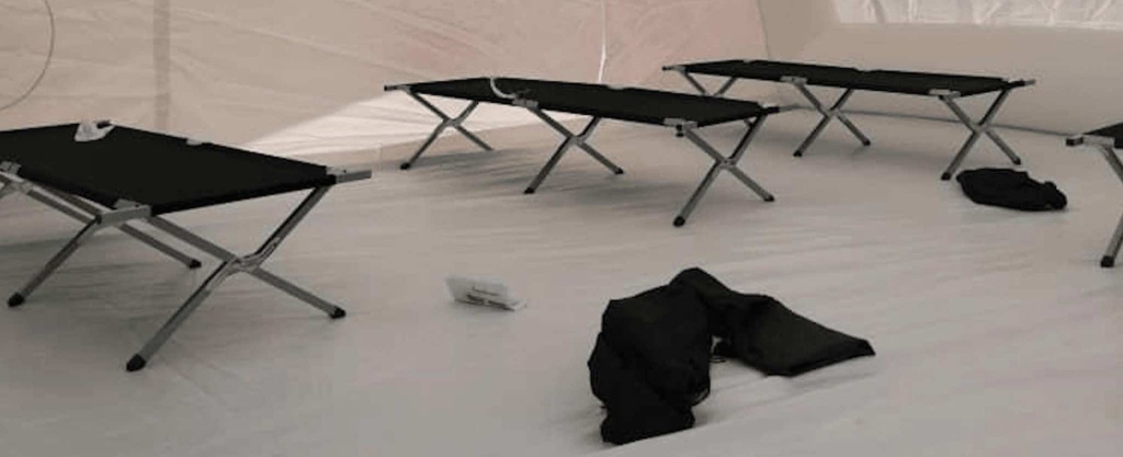 A detailed view of adult-sized folding cots, laid out on the ground on the tarpaulin inside the inflatable first aid shelter. We also supply this type of accessory to complement the inflatable tent. These cots are foldable, strong, and robust, and once folded and stored, they take up little space in an emergency vehicle; they are also lightweight. – Copyright Vivien LAÏLLE / FlyPix – All rights reserved, reproduction prohibited.