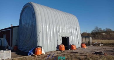The inflatable hangar is arranged in an inverted U-shape, secured by guy lines to sand-filled ballast bags. The side access door is visible. The 0.6 mm double-skinned, padded PVC walls are very robust and strong. – All rights reserved, copyright FLYPIX.