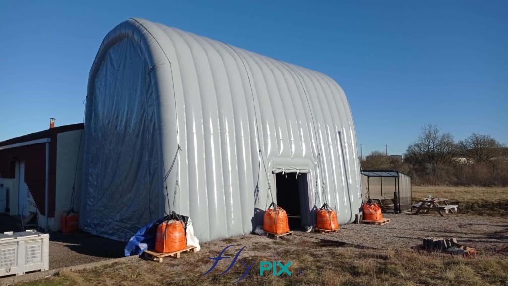 The inflatable hangar is arranged in an inverted U-shape, secured by guy lines to sand-filled ballast bags. The side access door is visible. The 0.6 mm double-skinned, padded PVC walls are very robust and strong. The inflatable hangar is arranged in an inverted U-shape, secured by guy lines to sand-filled ballast bags. The side access door is visible. The 0.6 mm double-skinned, padded PVC walls are very robust and strong. – All rights reserved, copyright FLYPIX.