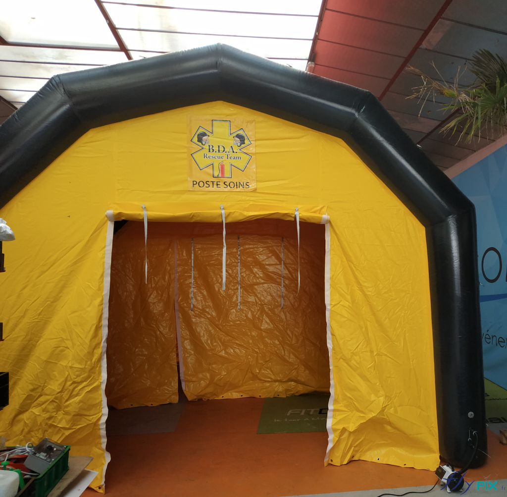 A front view of the PMA tent: wide gable door with Velcro fasteners, printed marking banner, Velcro fasteners above the door, black air-trapped frame tubes, inflated with an electric pump. – All rights reserved, reproduction prohibited. Copyright FlyPix / Vivien LAÏLLE.