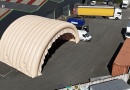 In this aerial photograph taken during an inflation and pressurization test before shipment to the client, you can see two assembled and connected half-moon tunnel modules, part of a large inflatable military hangar composed of five modules in total. Here, we have inflated the front gable module and an intermediate module. This large, wide, and tall mobile inflatable military hangar, designed for multiple uses, protects equipment and personnel from the elements during wartime. It will be deployed in military operations areas in armed conflict zones to accommodate soldiers, military personnel, paratroopers, and officers, as well as to store equipment, military vehicles, armored vehicles, tanks, aircraft, helicopters, and more. This inflatable structure, custom-made by us in our workshops in Orléans, France, is continuously inflated by several electric turbines. The inflatable shelter is entirely made of 0.45 mm double-skinned padded PVC, and features large doors, windows, and useful interfaces such as air sleeves for climate control inside the inflatable tent, and electrical cable sleeves, service doors and additional access for military personnel… – Copyright: Vivien LAÏLLE/FLYPIX, all rights reserved.
