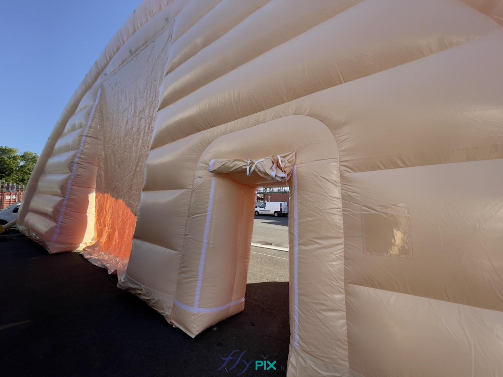 General view of the front gable end of the first module of the inflatable military hangar, shaped like a half-moon tunnel, with the small service door in the foreground on the right, and then in the background, in the center, the large, wide gable end door. - Copyright: Vivien LAÏLLE/FLYPIX, all rights reserved. General view of the front gable end of the first module of the inflatable military hangar, shaped like a half-moon tunnel, with the small service door in the foreground on the right, and then in the background, in the center, the large, wide gable end door. – Copyright: Vivien LAÏLLE/FLYPIX, all rights reserved.