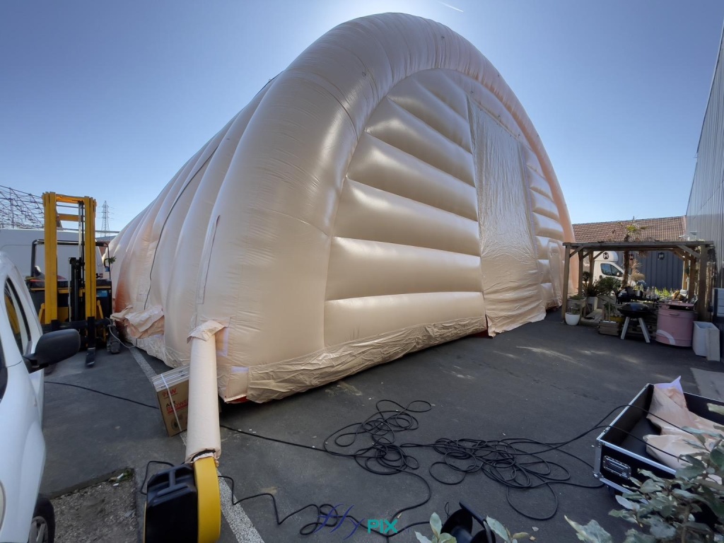 The inflatable military hangar, made of 0.45 mm double-skinned, padded PVC, is inflated with air by an electric turbine, visible in the lower left of this photograph. Air is supplied to the inflatable structure via an air sleeve attached to the turbine. The inflatable military hangar, made of 0.45 mm double-skinned, padded PVC, is inflated with air by an electric turbine, visible in the lower left of this photograph. Air is supplied to the inflatable structure via an air sleeve attached to the turbine. This photo clearly shows the process; the turbine must continuously supply air to the frame tubes and the walls of the inflatable shelter. – Copyright: Vivien LAÏLLE/FLYPIX, all rights reserved.