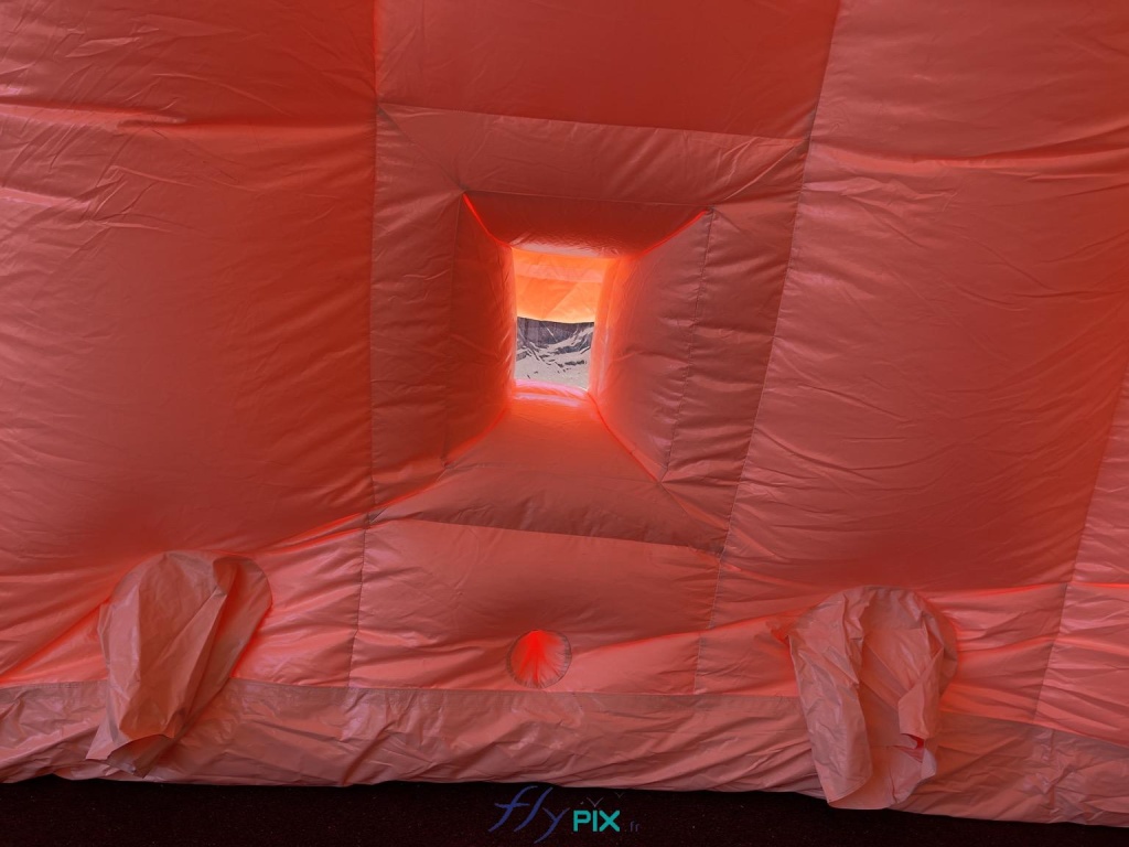 A view taken from inside the large inflatable hangar, showing several interfaces: a transparent window with a removable flap, positioned in the center of this photo. Below, in the center, is a hole for routing electrical wires and conduits. Then, to the right and left at the bottom, are two air vents for climate and air quality control inside the inflatable tent (air conditioning, heating, air filtration). The vents can also be used to route electrical cables if needed. - Copyright: Vivien LAÏLLE/FLYPIX, all rights reserved. A view taken from inside the large inflatable hangar, showing several interfaces: a transparent window with a removable flap, positioned in the center of this photo. Below, in the center, is a hole for routing electrical wires and conduits. Then, to the right and left at the bottom, are two air vents for controlling the climate and air quality inside the inflatable tent (air conditioning, heating, air filtration). The vents can also be used to route electrical cables if needed. – Copyright: Vivien LAÏLLE/FLYPIX, all rights reserved.