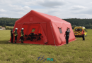 A simulation view showing the deployment of a 37 m² PMA tent, a captive air inflatable structure inflated with an electric pump. Deployment in a rural area. This inflatable shelter has a 0.6 mm single-layer PVC shell for the airtight inflatable tube frames, and a 0.45 mm single-layer PVC shell for the walls and roof. This inflatable tent is easy to set up and deploy, and when folded, it takes up very little space in the intervention vehicle. A removable groundsheet allows for deployment on a clean and dry surface. – This image was AI-generated using GEMINI, based on 3D model views of the final artwork created by our graphic designer and approved by the client, as well as photos and real-life shots of certain details of the inflatable tent, taken directly in our manufacturing workshop. Media partially generated by AI and verified by an agent. – Copyright Vivien LAÏLLE/FlyPix, all rights reserved, reproduction prohibited.