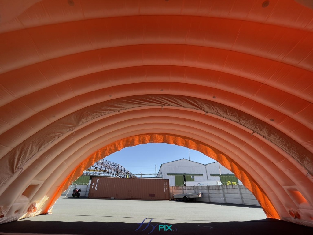 The inflatable hangar is composed of five modules which, once connected, assembled, and sealed, provide a very large volume and workspace. Its generous height and width allow for great versatility in the use of this military inflatable hangar. The inflatable modules can be arranged with or without gable ends, at one or more military sites, depending on operational needs in the field. - Copyright: Vivien LAÏLLE/FLYPIX, all rights reserved. The inflatable hangar is composed of five modules, which, once connected, assembled, and sealed, provide a very large volume and workspace. Its generous height and width allow for great versatility in the use of this military inflatable hangar. The inflatable modules can be arranged with or without gable ends, at one or more military sites, depending on operational needs in the field. – Copyright: Vivien LAÏLLE/FLYPIX, all rights reserved.