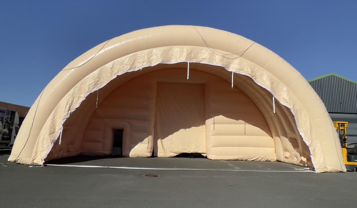 A general view taken from the ground, showing an inflatable tent module in the shape of a half-moon tunnel. This shape is very stable and robust because it provides good natural buttresses, with a keystone, and walls that effectively distribute the loads of the inflatable structure to the ground. Just like cathedrals. – Copyright: Vivien LAÏLLE/FLYPIX, all rights reserved.