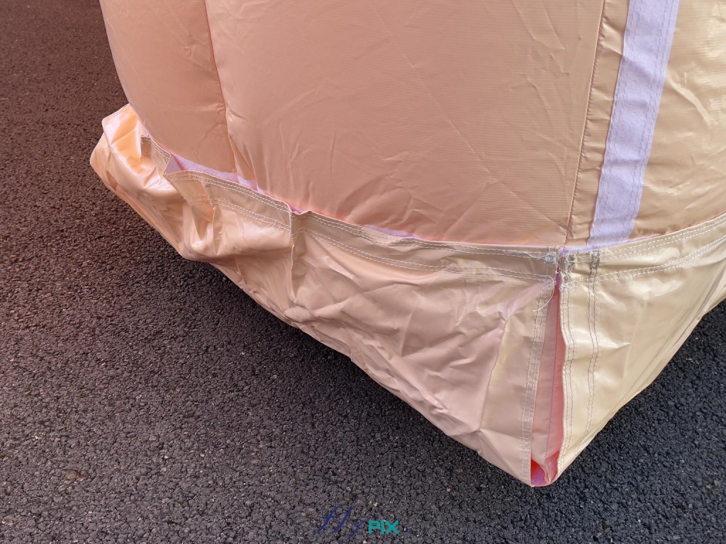 Beneath each inflatable hangar module, in contact with the ground, is a second skin: a removable 0.45 mm PVC protective cover secured with Velcro strips. This solution is ideal for protecting the inflatable tubes and walls in contact with the ground, minimizing abrasion over time. Beneath each module of the inflatable hangar, in contact with the ground, is a second skin: a removable 0.45 mm PVC protective cover secured with Velcro strips. This solution is ideal for protecting the inflatable tubes and walls in contact with the ground, limiting abrasion over time. This second skin is crucial because the inflatable military hangar is designed to be deployed on various types of terrain and surfaces (sand, concrete, gravel, rocks, asphalt, etc.). The removable covers also protect against sharp objects on the ground (iron objects, spikes, nails, etc.). The modules are thus protected. – Copyright: Vivien LAÏLLE/FLYPIX, all rights reserved.