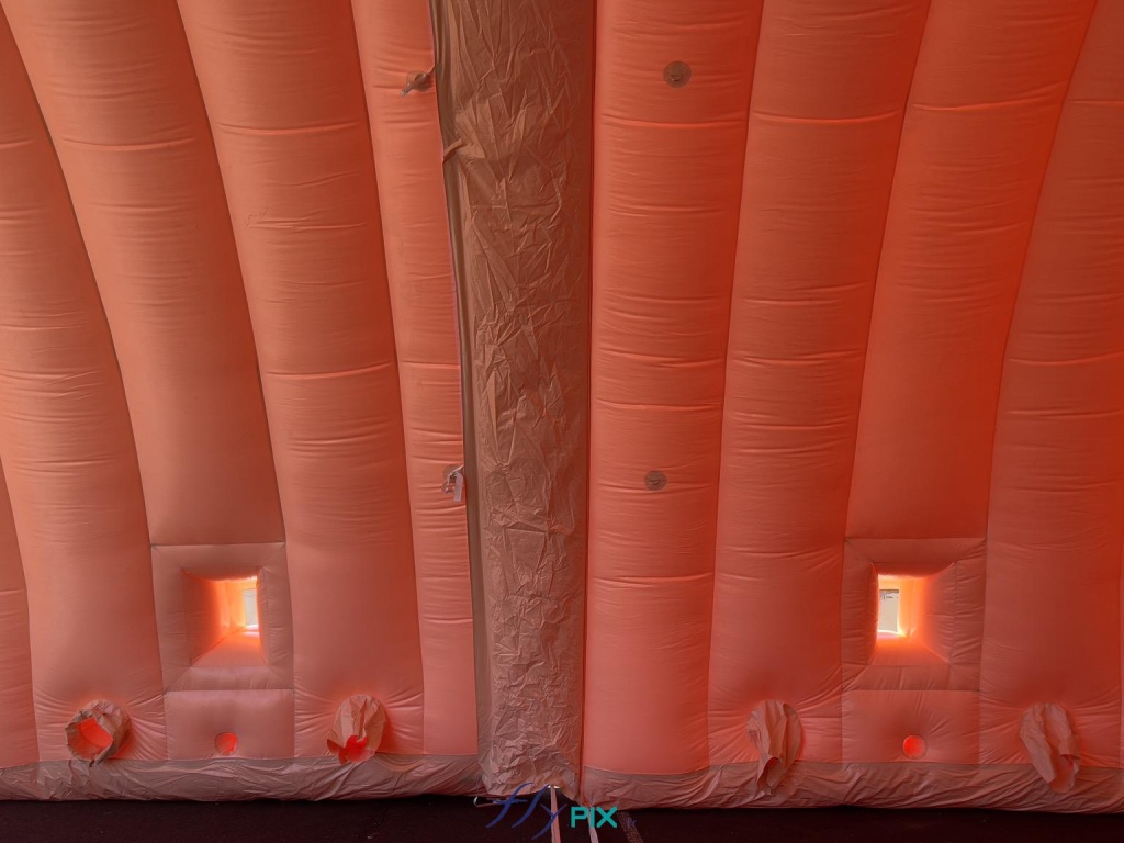 In this photo, two modules are assembled and sealed, with transparent windows and foldable, removable shutters that allow natural light to enter the inflatable hangar module. The lower sections of the inflatable modules show the air sleeves and the openings for electrical cables and conduits. - Copyright: Vivien LAÏLLE/FLYPIX, all rights reserved. In this photo, two modules are assembled and sealed, with transparent windows and foldable, removable shutters that allow natural light to enter the inflatable hangar module. In the lower sections of the inflatable modules, we can see the air sleeves and the openings for electrical cables and conduits. – Copyright: Vivien LAÏLLE/FLYPIX, all rights reserved.