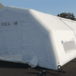Above: a general view of the inflatable first aid post shelter, measuring L = 10 m x W = 6 m, for a usable interior area of ​​S = 60 m². This photo shows the rear gable end of the inflatable first aid post tent, with a large exit door. The roof walls feature windows and skylights with mosquito netting, transparent PVC, and removable shutters. This is a sealed-air tent, meaning the 0.6 mm single-layer PVC inflatable frame tubes are airtight and are inflated with an electric pump via a non-return valve and pressure regulator. There is an air sleeve to the left and right of the door.