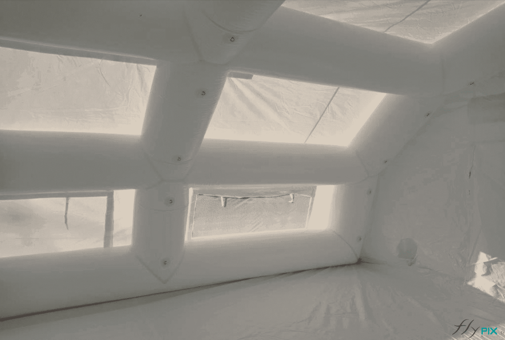 A photo shows the details and finish of the inflatable frame tubes and windows that act as skylights, illuminating the interior of the PMA inflatable tent with natural, diffused light. A removable, washable PVC groundsheet provides doctors and nurses with a healthy, dry, and temperature-controlled indoor environment. The interconnected frame also features metal rings and eyelets, offering practical and ergonomic interfaces for attaching medical equipment or LED lights.