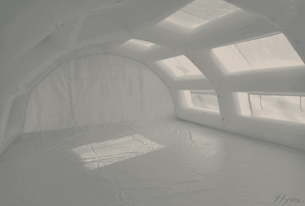 A view of the interior of the PMA inflatable tent, with a surface area of ​​60 m², and a removable PVC groundsheet. The frame tubes, the skeleton of the inflatable shelter, provide exceptional strength and robustness to the structure. They are all interconnected and feature regularly spaced metal rings and eyelets for attaching medical equipment or LED lighting devices. Note that the white PVC shell and the presence of skylights and windows allow for natural, diffused interior light.