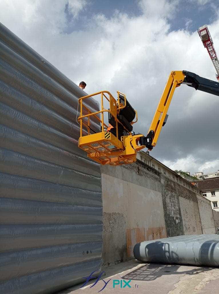 Aboard a crane-lifted platform, a technician fine-tunes the mountings and installation of noise barriers at an urban construction site in Paris. Our team handles the installation of inflatable noise-reduction barriers and also provides training. – All rights reserved; reproduction prohibited. Copyright FlyPix / Vivien LAÏLLE.